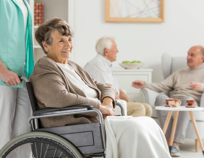 A woman in a wheelchair with two other people sitting on the couch.