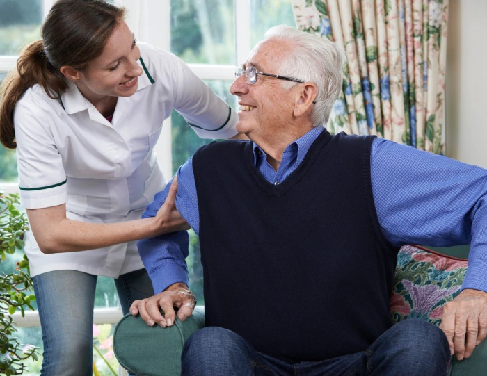 A woman helping an older man sit on the couch